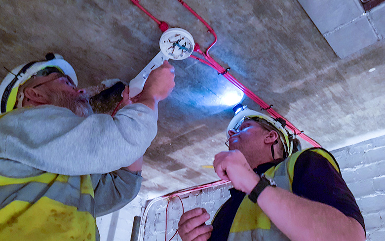 Two men installing Scorpion device to a detector in a lift shaft